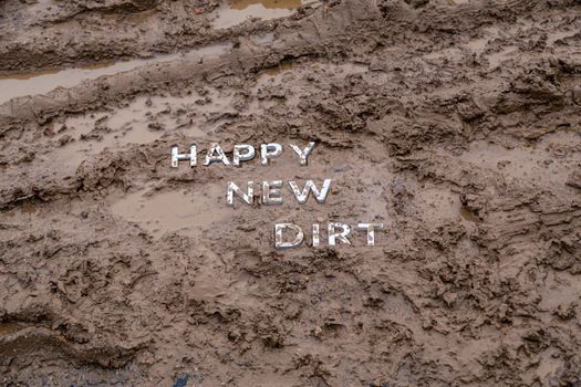 the words happy new dirt laid with silver metal letters on wet mud surface in diagonal perspective under cloudy autumn day light