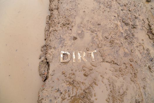 the word mud imprinted in wet dirt road surface and puddle - close-up with selective focus in flat lay perspective.
