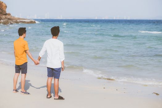 Back view homosexual young asian couple standing together on beach in summer, asia gay holding hands going sea for leisure and relax with romantic and happy in vacation at sea, LGBT with legal concept.