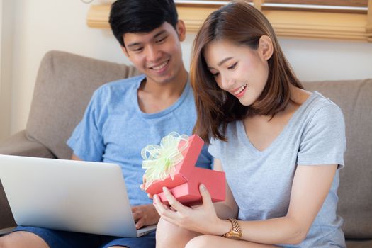 Young asian couple celebrate birthday together, asia man giving gift box present to woman for surprise at living room, female feeling happy and excited anniversary, holiday valentine concept.