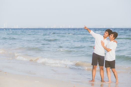 Homosexual portrait young asian couple standing pointing something together on beach in summer, asia gay going sea for leisure with romantic and happy in vacation at sea, LGBT with legal concept.