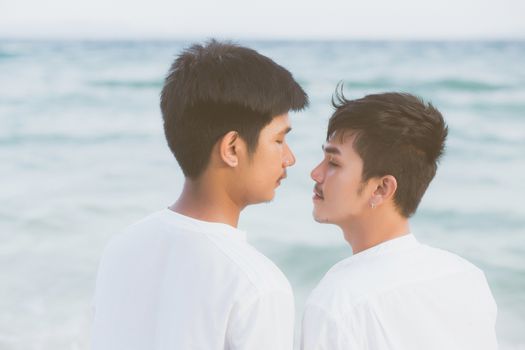 Back view homosexual young asian couple standing together on beach in summer, asia gay holding hands going sea for leisure and relax with romantic and happy in vacation at sea, LGBT with legal concept.