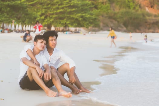 Homosexual portrait young asian couple sitting hug together on beach in summer, asia gay going tourism for leisure and relax with romantic and happiness in vacation at sea, LGBT legal concept.