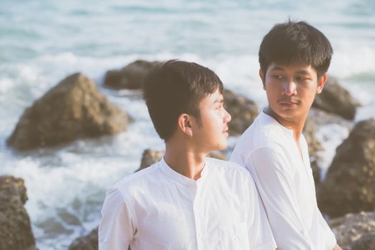 Homosexual portrait young asian couple sitting hug together on rock or stone in the beach in summer, asia gay going tourism for leisure and relax with happy in vacation at sea, LGBT legal concept.