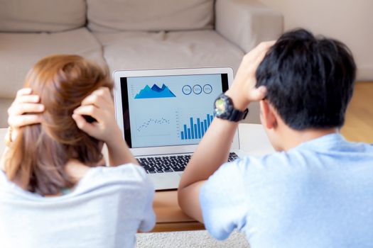 Young asian couple stressed and worried about finance of problem business together, man and woman looking laptop and frustrated about graph and report, family unhappy, lifestyle concept, back view.