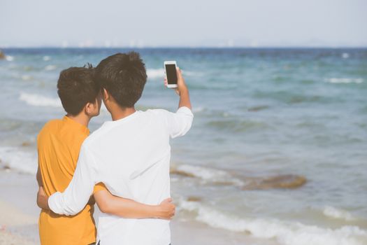 Back view gay portrait young couple smiling taking a selfie photo together with smart mobile phone at beach, LGBT homosexual lover in the vacation at sea, two man going to travel, holiday concept.