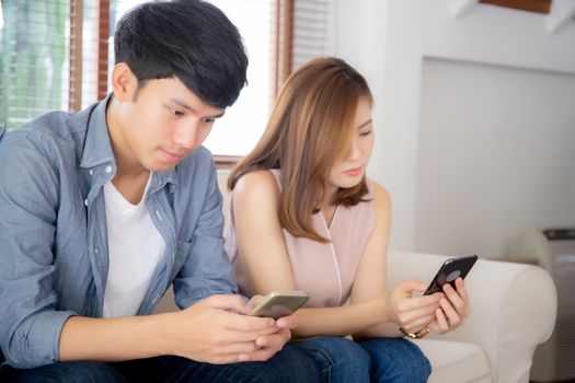 Young asian couple sitting on sofa with problem about relationship because addicts social network media together, asia family expression with looking phone with ignoring and indifferent.