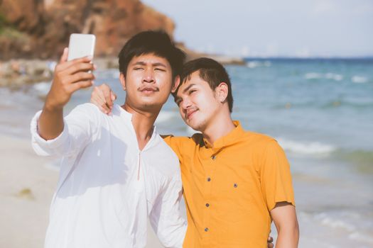 Gay portrait young couple smiling taking a selfie photo together with smart mobile phone at beach, LGBT homosexual lover in the vacation at sea, two man going to travel, holiday concept.