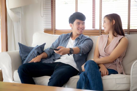 Beautiful young asian couple holding remote and watching tv or video streaming on sofa with relax and happy in living room at home, lifestyle family leisure with entertainment enjoy together on couch.