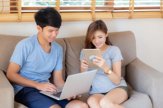 Beautiful young asian couple cheerful freelance working with man using laptop and woman using tablet on couch, family relax and sharing communication together at home, lifestyle concept.