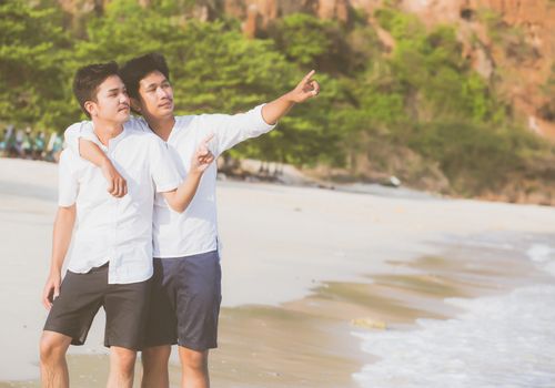 Homosexual portrait young asian couple standing pointing something together on beach in summer, asia gay going sea for leisure with romantic and happy in vacation at sea, LGBT with legal concept.