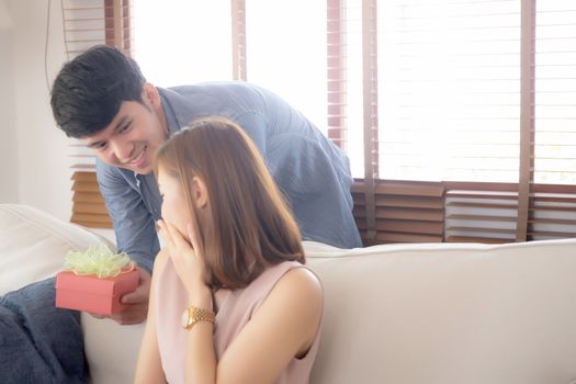 Young asian couple celebrate birthday together, asia man giving gift box present to woman for surprise at living room, female feeling happy and excited anniversary, holiday valentine concept.