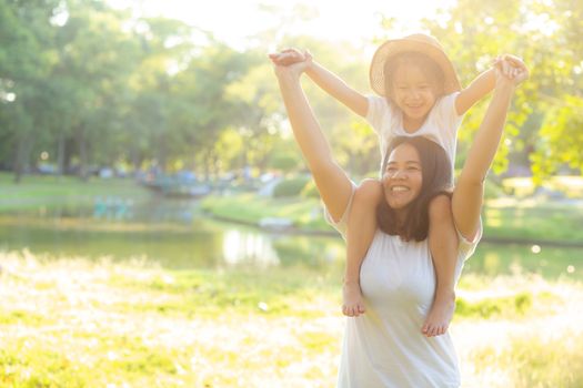 Beautiful young asian mother carrying little daughter with smile, child ride the neck on mom with happiness and cheerful together in the park, lifestyle family with enjoy and fun concept.