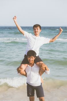 Homosexual portrait young asian couple riding the neck together with enjoy and fun on beach in summer, asia gay cheerful going sea for leisure with romantic and happy vacation at sea, LGBT with legal.