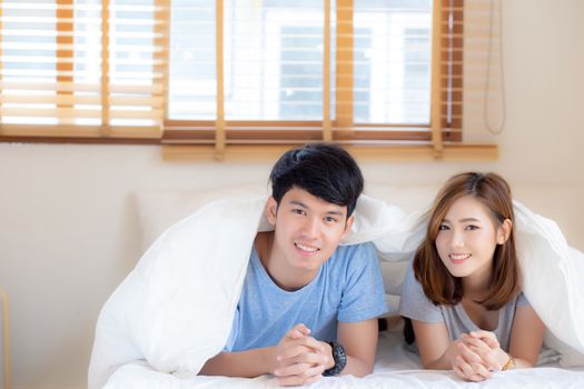 Beautiful portrait young asian couple relax and satisfied together in bedroom at home, family lying on bed confident with cheerful and happy with relationship, man and woman dating.
