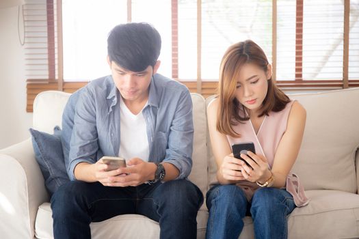 Young asian couple sitting on sofa with problem about relationship because addicts social network media together, asia family expression with looking phone with ignoring and indifferent.