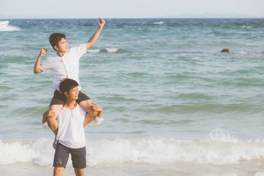 Homosexual portrait young asian couple riding the neck together with enjoy and fun on beach in summer, asia gay cheerful going sea for leisure with romantic and happy vacation at sea, LGBT with legal.