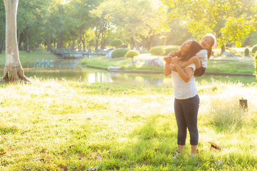 Beautiful young asian mother carrying little daughter with smile, child ride the neck on mom with happiness and cheerful together in the park, lifestyle family with enjoy and fun concept.