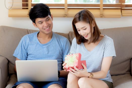 Young asian couple celebrate birthday together, asia man giving gift box present to woman for surprise at living room, female feeling happy and excited anniversary, holiday valentine concept.