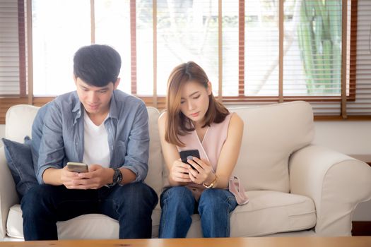 Young asian couple sitting on sofa with problem about relationship because addicts social network media together, asia family expression with looking phone with ignoring and indifferent.