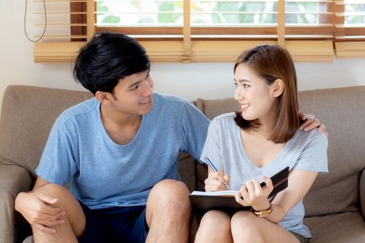 Beautiful young asian couple planning and writing on notepad or diary, family list purchase, man and woman cheerful studying and read for education, family relax, lifestyle and wellbeing concept.