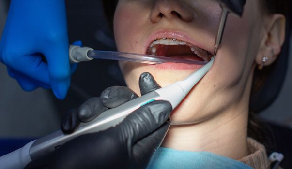 A woman with dental braces visits an orthodontist at the clinic. in the dental chair during the procedure of installing braces on the upper and lower teeth. Dentist and assistant work together, they have dental instruments in their hands. concept of dentistry