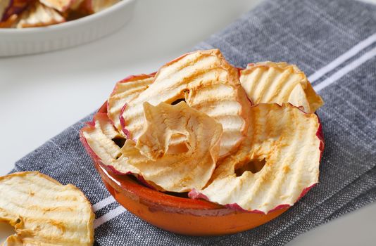Bowl of dried apple slices - apple chips or rings - on gray napkin