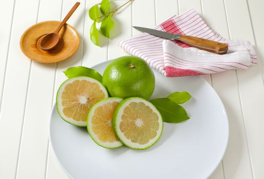 Sweetie fruit (green grapefruit, pomelit) - whole fruit and slices - on white plate