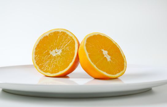 Two fresh orange halves on white plate