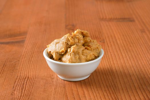 Crunchy peanut butter in white bowl on wooden background