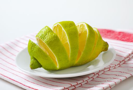 Lemon with green peel and yellow flesh, sliced on white plate