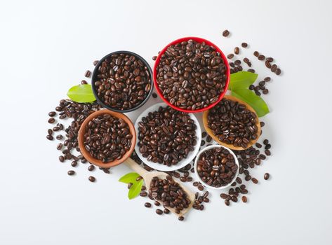 Roasted coffee beans in various bowls, on plate and wooden scoop