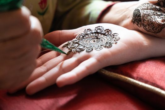 Top down video of a woman copying the mehndi henna tattoo from one hand to the other in preparation of the hindu festival of teej, karwachauth, diwali dussera or a marriage function. Shot in natural light on a beautiful red background it shows the amazing artistry of make up artists who make these beautiful and intricate designs