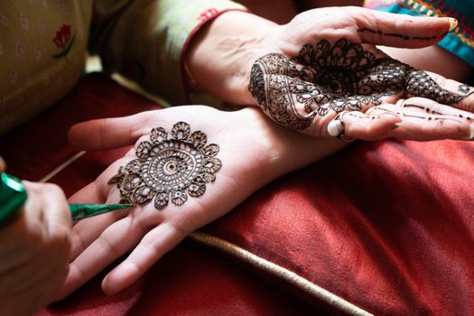 Top down video of a woman copying the mehndi henna tattoo from one hand to the other in preparation of the hindu festival of teej, karwachauth, diwali dussera or a marriage function. Shot in natural light on a beautiful red background it shows the amazing artistry of make up artists who make these beautiful and intricate designs