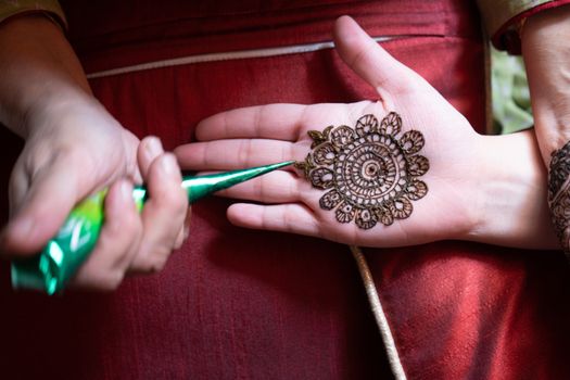 Top down video of a woman copying the mehndi henna tattoo from one hand to the other in preparation of the hindu festival of teej, karwachauth, diwali dussera or a marriage function. Shot in natural light on a beautiful red background it shows the amazing artistry of make up artists who make these beautiful and intricate designs