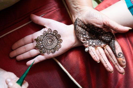 Top down video of a woman copying the mehndi henna tattoo from one hand to the other in preparation of the hindu festival of teej, karwachauth, diwali dussera or a marriage function. Shot in natural light on a beautiful red background it shows the amazing artistry of make up artists who make these beautiful and intricate designs