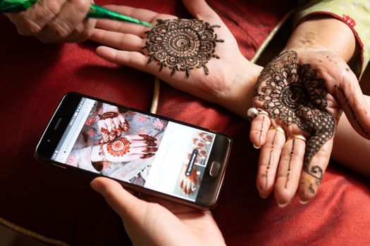 Woman getting a henna tattoo mehendi design copied from phone onto her hand for the bride bridesmaid shaadi event or a hindu festival like karwachauth diwali holi and teej. Shows the very popular temporary tattoo method that is a part of the hindu religion and is widely done across india