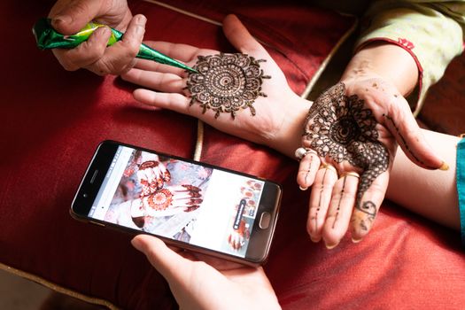 Woman getting a henna tattoo mehendi design copied from phone onto her hand for the bride bridesmaid shaadi event or a hindu festival like karwachauth diwali holi and teej. Shows the very popular temporary tattoo method that is a part of the hindu religion and is widely done across india