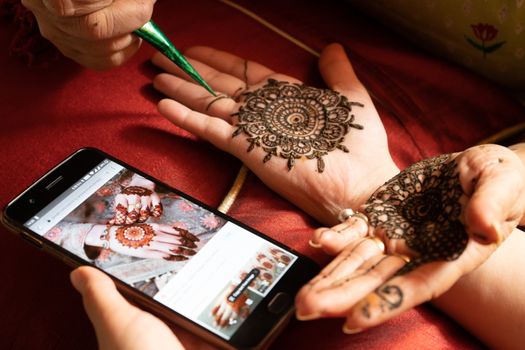 Woman getting a henna tattoo mehendi design copied from phone onto her hand for the bride bridesmaid shaadi event or a hindu festival like karwachauth diwali holi and teej. Shows the very popular temporary tattoo method that is a part of the hindu religion and is widely done across india