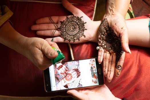 Woman getting a henna tattoo mehendi design copied from phone onto her hand for the bride bridesmaid shaadi event or a hindu festival like karwachauth diwali holi and teej. Shows the very popular temporary tattoo method that is a part of the hindu religion and is widely done across india