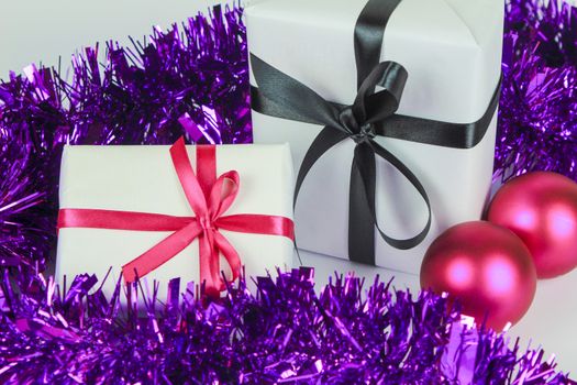Gifts wrapped with white paper and pink and black bows next to Christmas decoration on white background