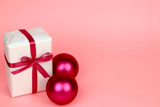 Gift wrapped with white paper and pink bow next to Christmas decoration on pink background