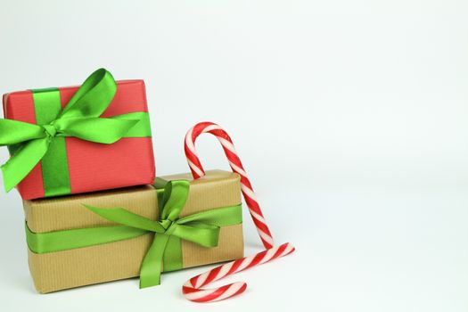 Gifts wrapped with brown and red paper and green bows next to Christmas decoration on white background