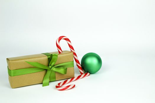 Gifts wrapped with brown paper and green bow next to Christmas decoration on white background