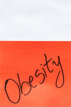 Obesity handwriting text close up isolated on orange paper with copy space. Writing text on memo post reminder