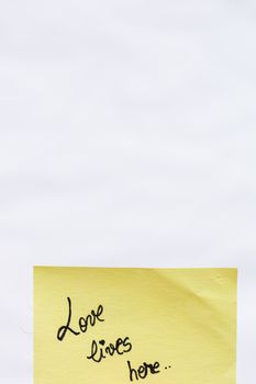 Love lives here handwriting text close up isolated on yellow paper with copy space.