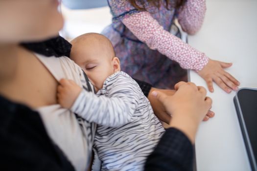 Sleeping baby peacefully resting in arms and holding the shirt of her mother who sits at a desk. Mother holding her slipping baby while using a laptop. Peacefully sleeping babies in arms