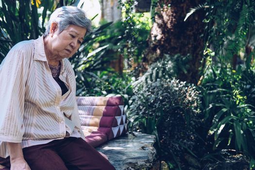 stressed depressed fatigued sad upset asian old asian elderly senior elder woman sitting in garden.