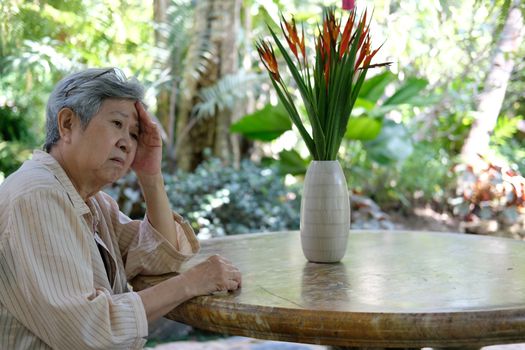 stressed depressed fatigued sad upset asian old asian elderly senior elder woman sitting in garden.