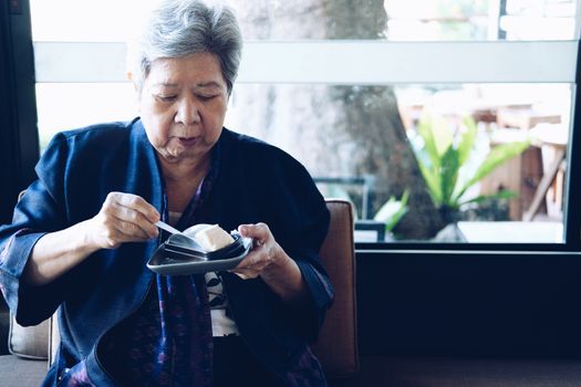 old asian elderly senior elder woman eating cheesecake at restaurant. mature retirement lifestyle